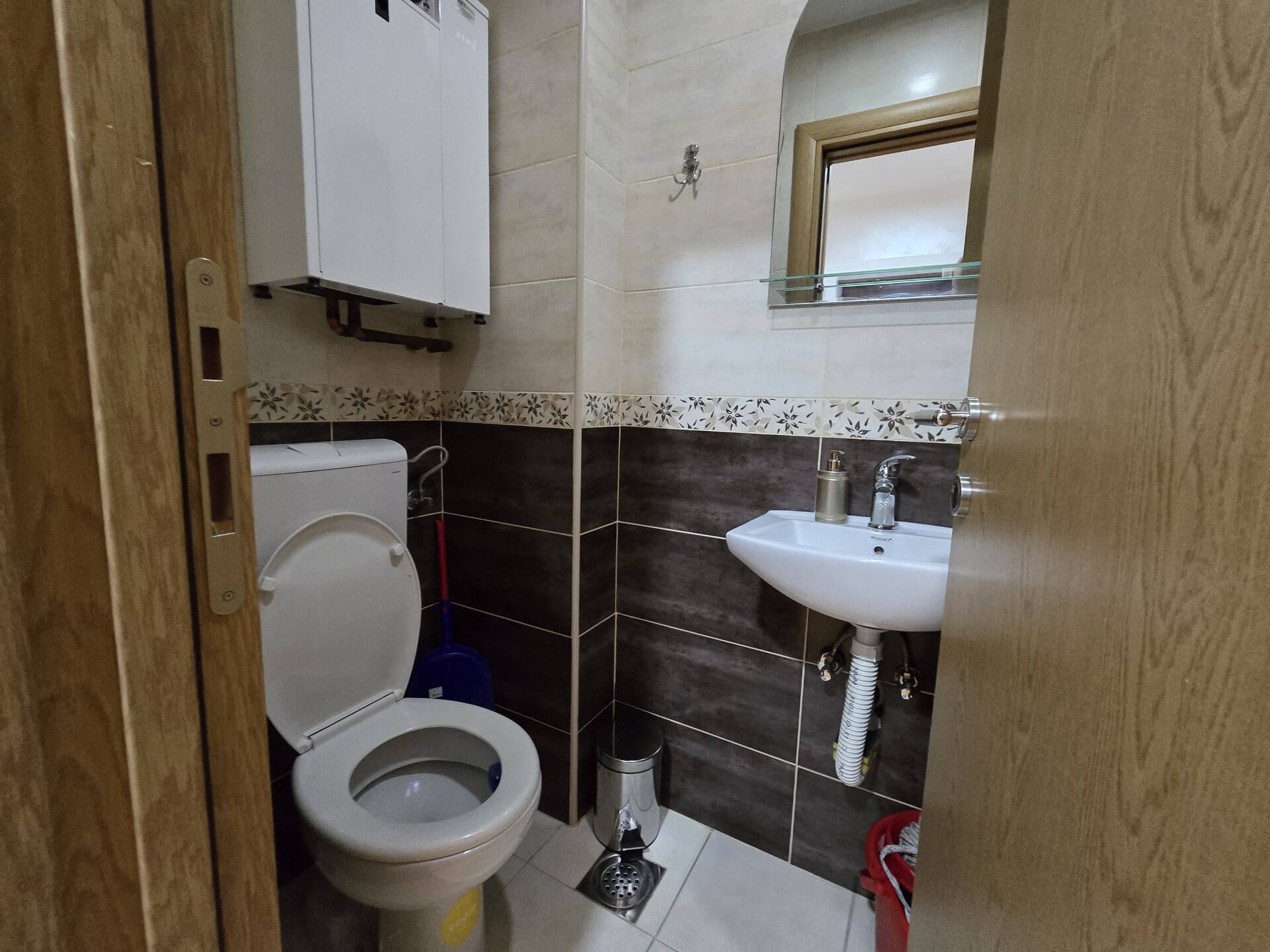 Toalet, wc šolja, umivaonik, kotao, a iza vrata se nalazi mašina za pranje i sušenje veša