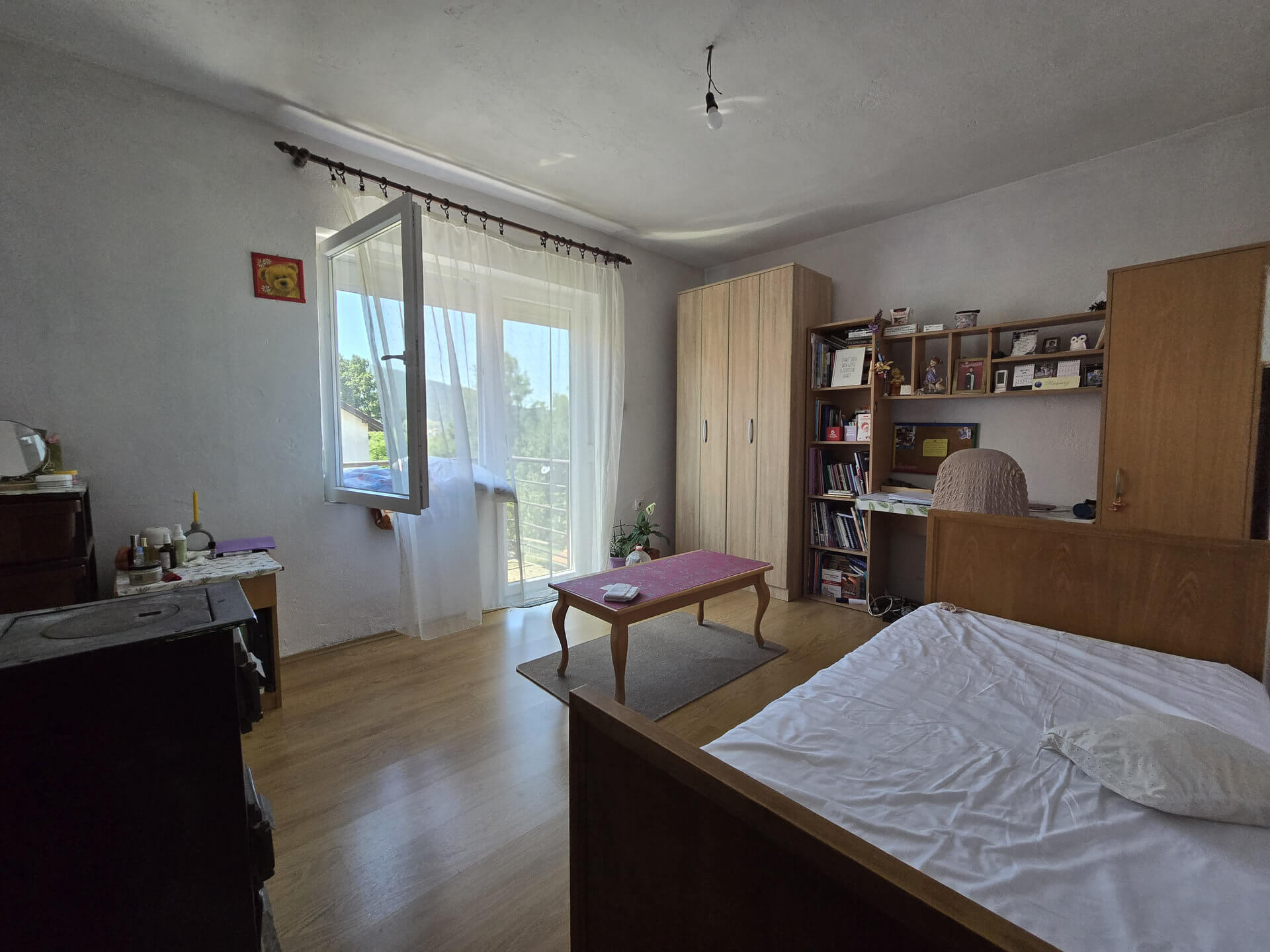 Još jedna spavaća soba, krevet, ormar i police, rozi sto na sredini, izlaz na terasu