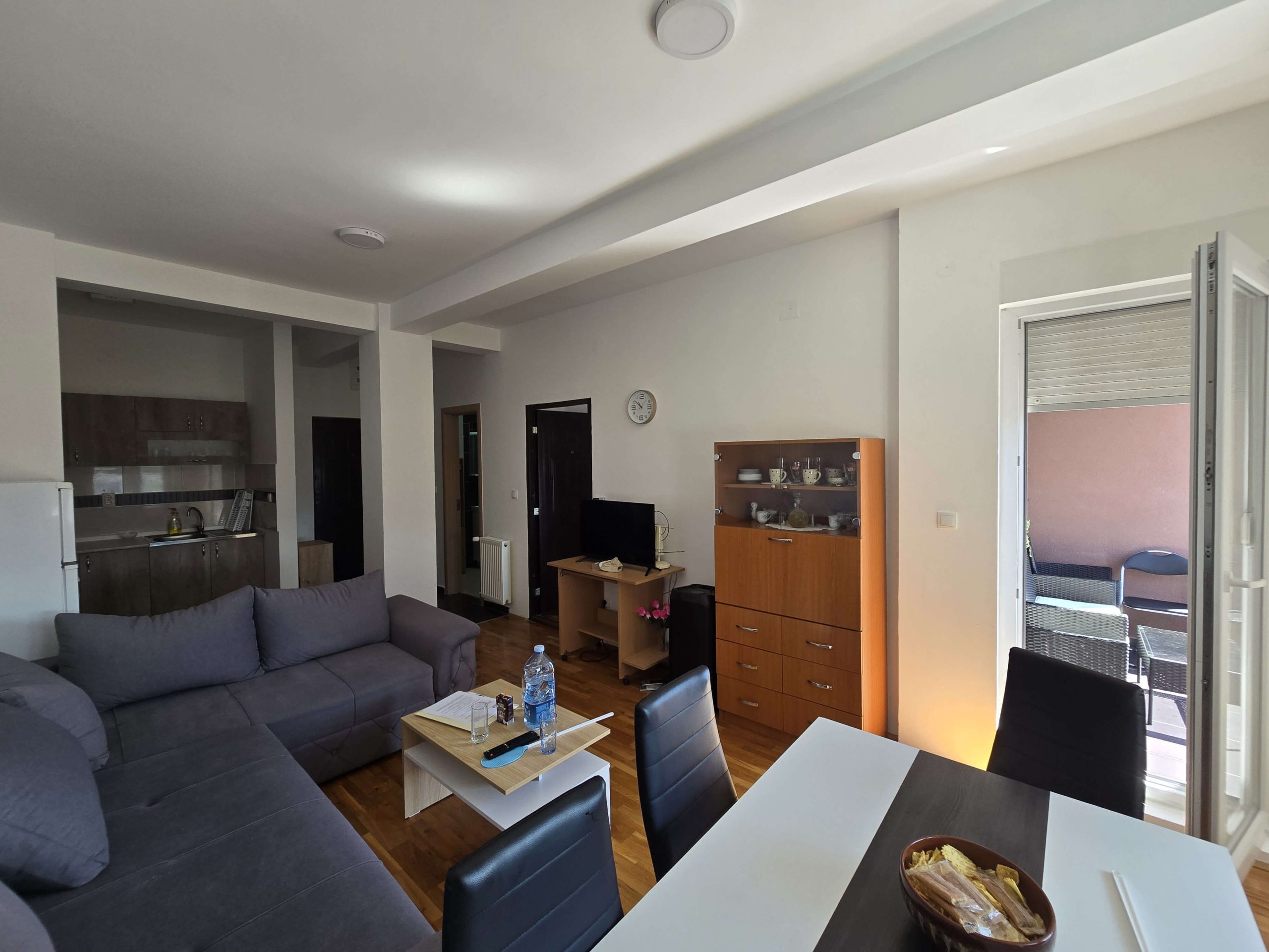 Dnevna doba iz drugog ugla, u prvom planu trpezarijski sto i stolice, klub sto, a u drugom planu kuhinja sa kupatilom